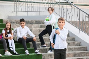 Şirin çocuk ve sınıf arkadaşları okulun yanındaki merdivenlerde oturuyorlar.