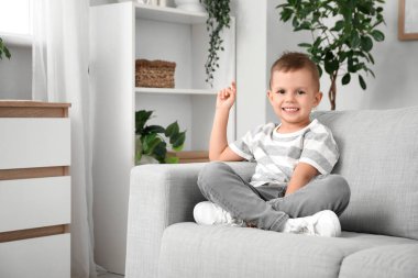 Evdeki kanepede oturan işaret parmağı kaldırılmış şirin küçük çocuk.