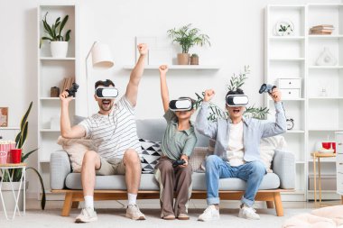 Mutlu bir baba ve VR gözlüklü çocukları evdeki kanepede oyun oynuyorlar.