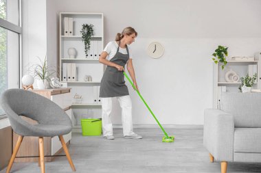 Kadın hademe odayı paspaslıyor.