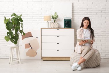 Oturma odasında nemlendiricisi olan taşınabilir yelpazenin yanında kitap okuyan güzel bir genç kadın.