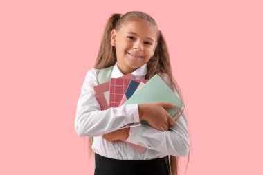 Okul üniformalı, pembe arka plan kitapları olan şirin bir kız.
