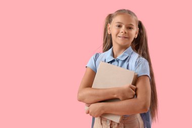 Pembe arka planda dizüstü bilgisayarı olan okul üniformalı şirin bir kız.