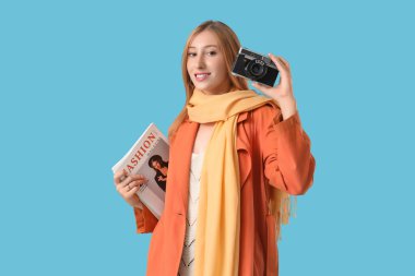 Mavi arka planda fotoğraf makinesi ve dergileri olan güzel genç bir kadın.