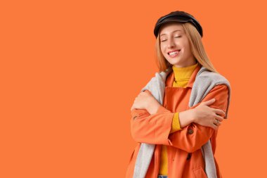 Turuncu arka planda süveteri olan güzel genç bir kadın.