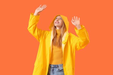 Turuncu arka planda yağmurluk giymiş güzel bir kadın.