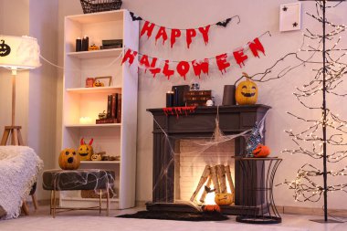 İçinde şömine, balkabağı ve Cadılar Bayramı süslemeleri olan karanlık bir oturma odası.