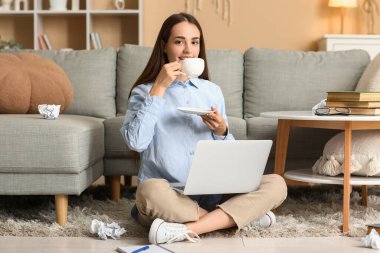 Dizüstü bilgisayarı, kitapları ve evde oturmuş çay içen mutlu kadın yazar.