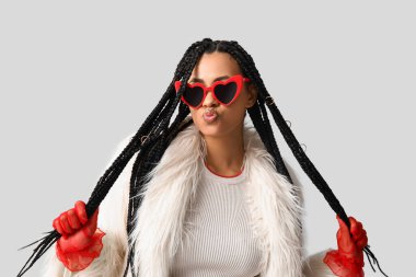 Hafif arka planda örgüleri olan şık bir Afro-Amerikan kadın.