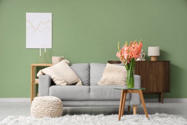 Oturma odasında, kanepe, puf ve gladiolus çiçekleri masanın üzerinde.