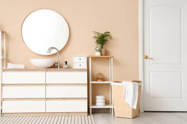 Lavabosu, çekmecesi ve bej duvarın yanında raf ünitesi olan şık bir banyo.