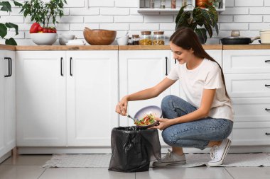 Mutfaktaki çöp kutusuna organik yiyecek atan genç bir kadın. Atık geri dönüşüm kavramı