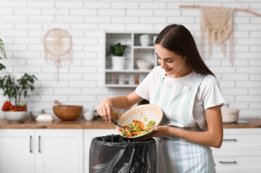Mutfaktaki çöp kutusuna organik yiyecek atan genç bir kadın. Atık geri dönüşüm kavramı