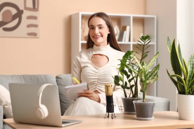 Not defteri ve bitkilerle evde podcast yapan genç bir kadın.