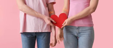 Blood donors with applied patches and paper heart on pink background, closeup