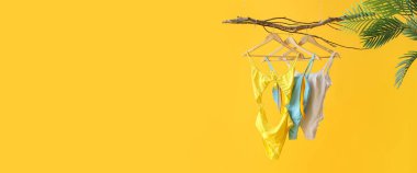 Ağaç dalında asılı farklı tarz mayolar sarı arkaplan ve metin için yer var. Yaz tatili kavramı