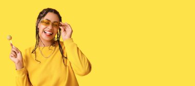 Sarı arka planda lolipop tutan mutlu Afro-Amerikalı kadın. Mesaj için yer var.