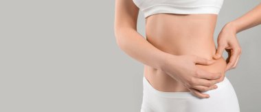 İç çamaşırlı genç bir kadın gri arka planda yağına dokunuyor mesaj için yeri var, yakın plan. Estetik ameliyat konsepti