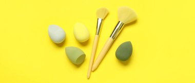 Sarı arka planda makyaj süngerleri ve fırçalar