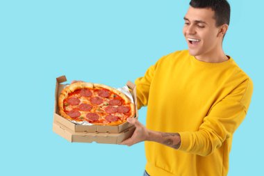 Mavi arka planda lezzetli biberli pizzalı genç adam.