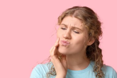 Pembe arka planda diş ağrısı çeken güzel bir genç kadın.