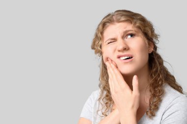 Gri arka plan üzerinde diş ağrısı muzdarip güzel genç kadın