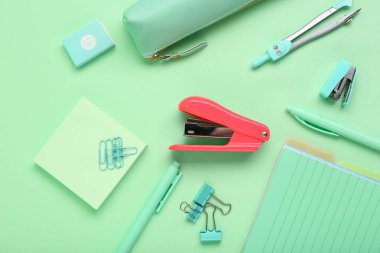 Yeşil arka planda zımba bulunan okul malzemeleri.