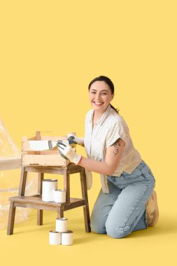 Sarı arka planda tahta kutu boyayan genç bir kadın.
