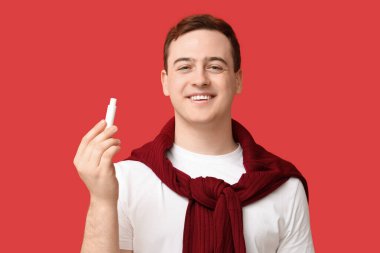 Kırmızı arka planda dudak merhemi olan mutlu genç adam.