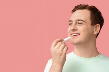 Yakışıklı genç adam pembe arka plana dudak kremi sürüyor.