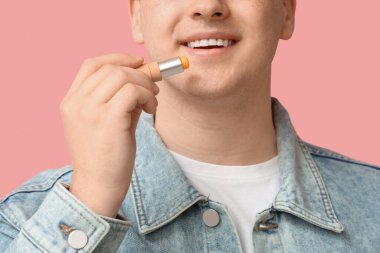 Genç adam pembe arka plana dudak kremi sürüyor, yakın plan.