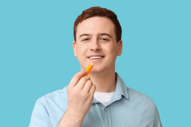 Yakışıklı genç adam mavi arka plana dudak kremi sürüyor.