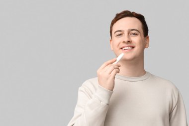 Gri arka plana dudak kremi süren yakışıklı genç adam.
