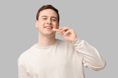 Gri arka planda dudak merhemi olan mutlu genç adam.