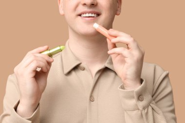 Kahverengi arka planda dudak kremi olan genç bir adam.