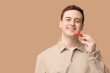 Kahverengi arka planda dudak kremi süren yakışıklı bir genç.