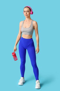 Mavi arka planda bir şişe su ve kulaklığı olan genç bir bayan antrenör.