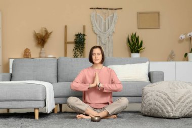Genç bir kadın evde yerde oturmuş meditasyon yapıyor.