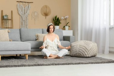 Genç bir kadın evde yerde oturmuş meditasyon yapıyor.