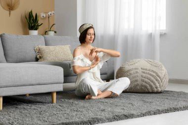 Genç bir kadın evde yerde oturmuş meditasyon yapıyor.