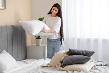 Genç bir kadın yatak odasına yastık koyuyor.