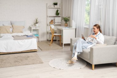 Kadın tıp öğrencisi, evdeki kanepede tabletle ders çalışıyor.