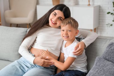 Çocuk oturma odasındaki kanepede annesinin karnına dokunuyor.