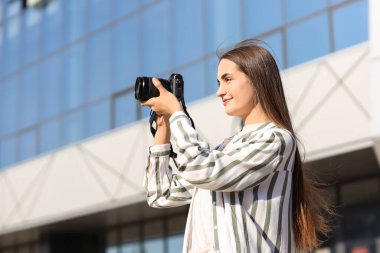 Modern kameralı genç bayan fotoğrafçı dışarıda fotoğraf çekiyor.