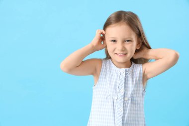 Pedikülozu olan küçük bir kız mavi arka planda başını kaşıyor.