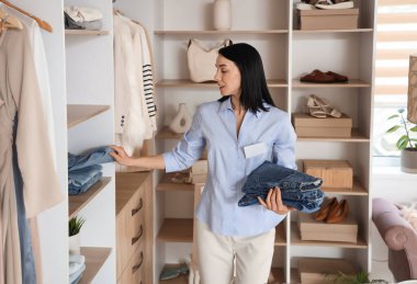 Kadın satıcı elbise mağazasındaki raftan katlanmış kot pantolon alıyor.