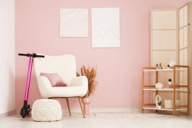 Oturma odasının içinde elektrikli scooter, koltuk ve raf ünitesi var.