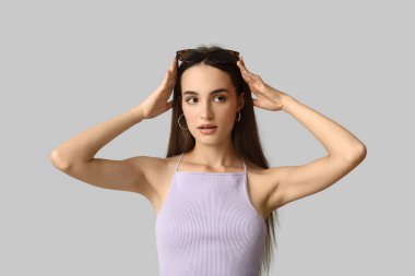 Gri arka planda şık güneş gözlüklü güzel bir genç kadın.