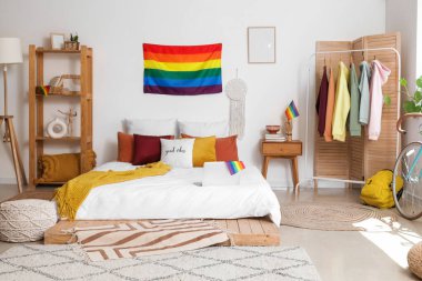 Yatak odasının içinde LGBT bayrakları, elbise askılığı ve raf ünitesi var.