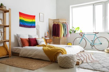 Yatak odasının içinde LGBT bayrakları, elbise askılığı ve bisiklet var.